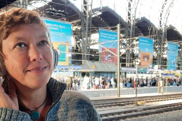 Autorin im Bahnhof hört Anweisungen von KI als Reisebuddy im Bahnhof